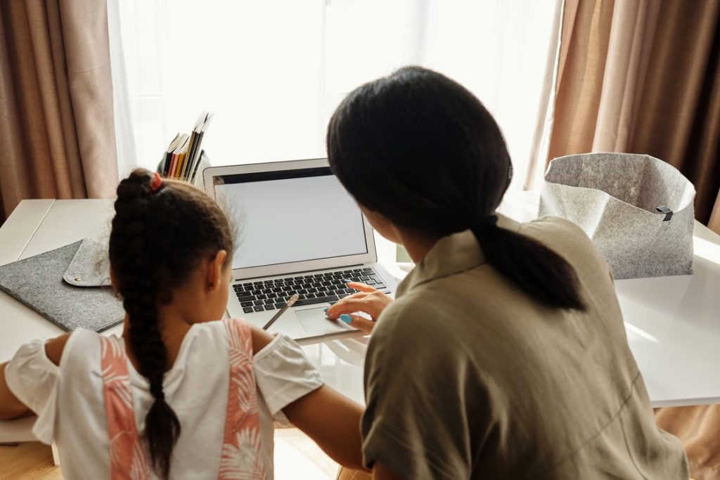 A mother helps her daughter with her homework on a computer screen.
