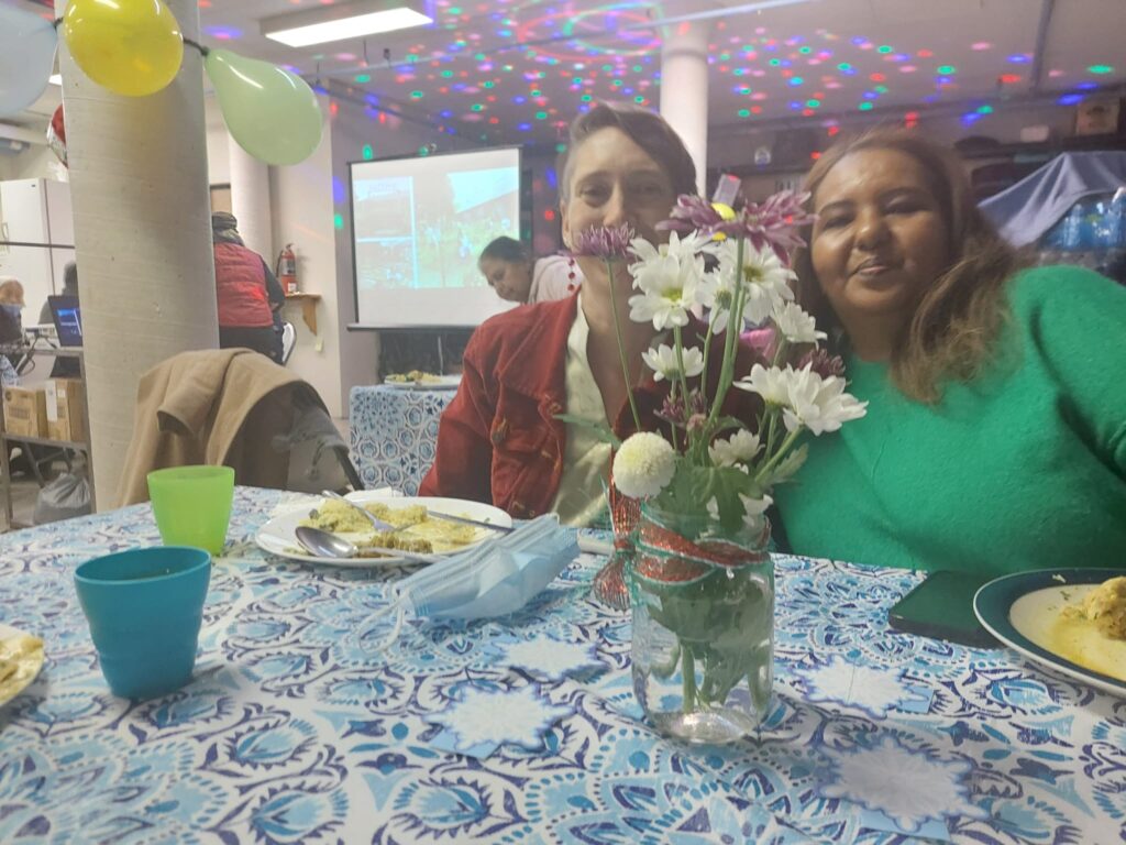 Two women sitting at a table with a flower vase.